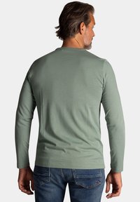 Lange mouw, mintgroene t-shirt van zachte stof. Heeft een ronde halslijn en een getsimde silhoeet, gecombineerd met donkere spijkerbroek.