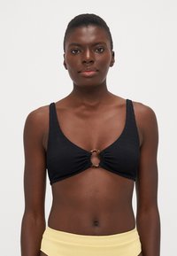Svart texturerad bikinitopp med en rund ringdetalj i mitten. Tjocka axelband och en konturerad form förbättrar passformen.