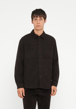 Black button-up shirt made of a soft, textured fabric. It features two chest pockets and a classic collar. The fit is relaxed.