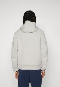 Sweatshirt in light gray with a hood, featuring a smooth, textured finish, ribbed cuffs, and a relaxed fit. No visible logos or patterns.