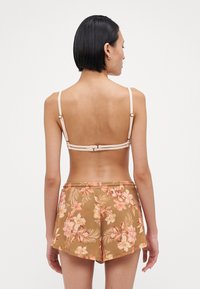 Bralette crème avec des bretelles amovibles, associé à un short floral marron orné de fleurs roses et oranges et d'un motif à rayures texturé.