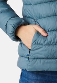 Isolierte Puffjacke in sanftem Blaugrün, mit gesteppten Paneelen, einer Reißverschlusstasche und einem Akzent in Blau und Gelb der schwedischen Flagge.
