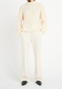 Pull-over en tricot crème avec un col montant, assorti à un pantalon beige clair sur mesure et des chaussures noires à bout pointu.
