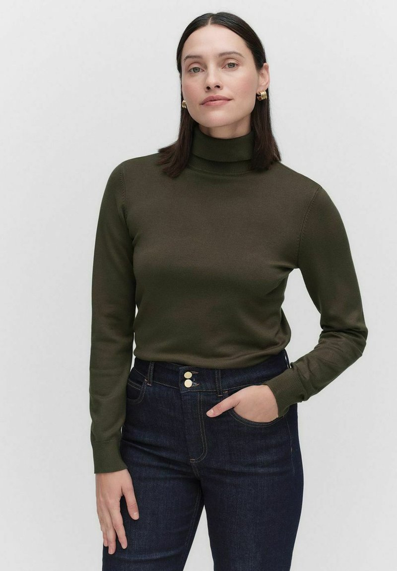 Olivgrön polotröja med långa ärmar, slät textur, figurnära design, i kombination med mörka jeans med knäppning i midjan.