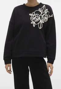 Sudadera negra con diseño de rosa blanca bordada en el pecho izquierdo. Presenta un ajuste holgado, cuello redondo y dobladillo y puños acanalados.