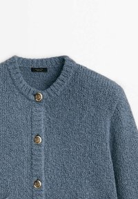 Cardigan bleu texturé avec un col rond, doté de quatre boutons dorés sur le devant. Fabriqué à partir d'un matériau tricoté doux.