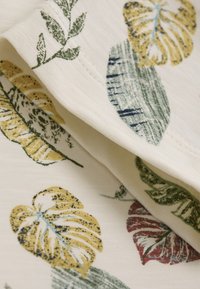 Let letstof med et botanisk print bestående af grønne, gule og røde blade på en cremefarvet baggrund. Tekstureret, blød overflade med lagdelt udseende.
