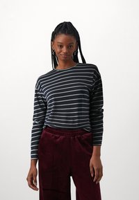 Sorte og hvite striper langermet skjorte med rund hals, sammen med burgunderfløyelsbukser med elastisk midje.