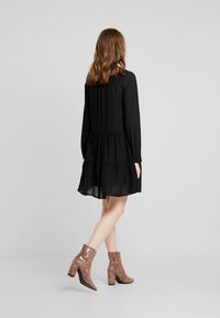 Černé, vrstvené šaty s dlouhými rukávy, vyrobené z průhledné látky. V páru s texturovanými růžovými kotníkovými botami s hadím potiskem a blokovým podpatkem.