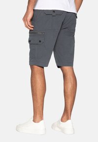 Bermudas grises con múltiples bolsillos, detalles de botón y cremallera, y un ajuste relajado, combinadas con zapatillas blancas.