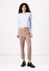 Haut à manches longues côtelé bleu clair avec un ourlet en dentelle, associé à un pantalon beige ajusté et des mocassins noirs épais. Fond de studio.