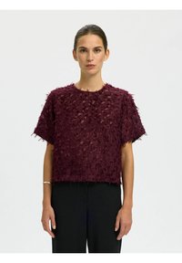 Bordeaux kortemouwen top met textuur en rafelige details; losse, boxy pasvorm; ronde halslijn; gecombineerd met zwarte broeken.
