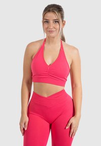 Roze sportieve crop top met halternekontwerp, voorzien van ruches aan de voorkant. Gepaarde met hoge taille, bijpassende leggings.
