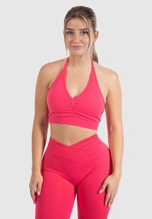 Roze sportieve crop top met halternekontwerp, voorzien van ruches aan de voorkant. Gepaarde met hoge taille, bijpassende leggings.