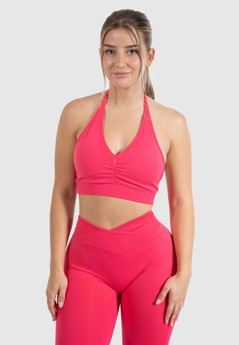 Top corto atlético rosa con un diseño de cuello halter, que presenta un detalle recogido en la parte delantera. Combinado con leggings de talle alto a juego.