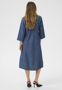 Jeansklänning med trekvartsärmar, åtsittande midja och en flödande kjol, med en medelblå tvätt och minimala sömnadsdetaljer.