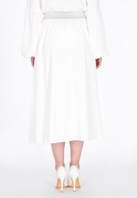 Witte vloeiende rok met een zilveren elastische tailleband. Draagt met witte hoge hakken, die een eenvoudige en gladde textuur laten zien.