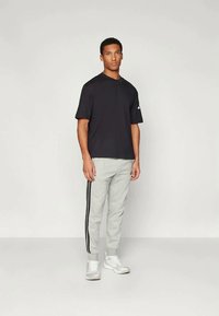 Crna majica kratkih rukava s okruglim izrezom, uparena sa svijetlosivim trenirkama s crnim bočnim prugama. Model stoji uspravno.