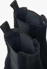 Czarne zamszowe botki za kostkę z elastycznymi panelami po bokach, prezentujące gładką fakturę i zaokrąglone otwory ułatwiające zakładanie. Brak widocznych elementów metalowych czy ozdobników.