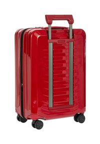 Valigia rigida rossa con scanalature verticali, manico retrattile e quattro ruote nere. Presenta una chiusura a zip lungo un lato.