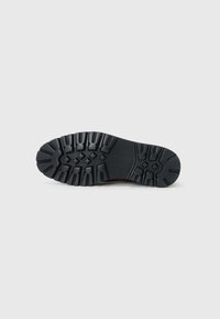 Suela de zapato de goma negra con huellas profundas y superficie texturada; presenta patrones angulares para agarre y estabilidad. Diseño de puntera redonda.