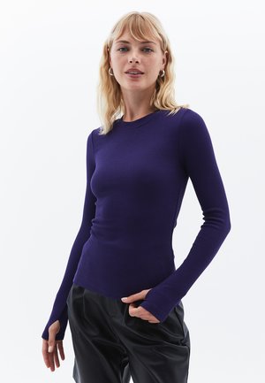 Paarse langemmouwen ribbeltop met een ronde halslijn en een aansluitend ontwerp. De lange mouwen hebben duimgaten. Model draagt zwarte broeken.