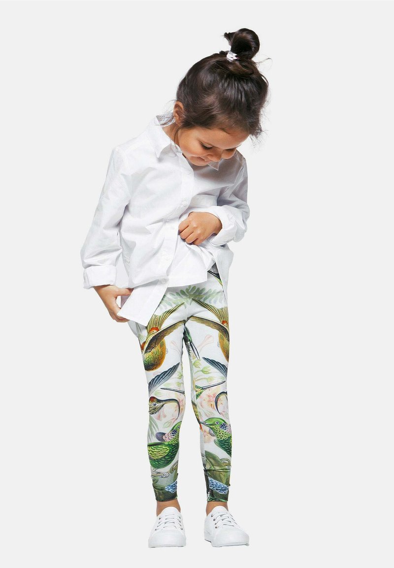 Leggings coloridos con un estampado detallado de aves y flores, combinados con una camisa blanca de botones y zapatos blancos, destacando patrones vibrantes.