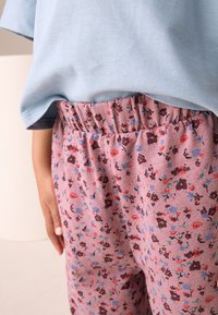 Camicia a maniche corte azzurro chiaro abbinata a pantaloni rosa con motivo floreale strutturato, dotati di cintura elastica e piccoli fiori decorativi.