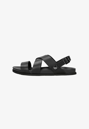 Black sandals made of synthetic material with cross straps, a round toe, and an adjustable buckle strap. Features a flat sole.