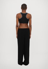 Black athletic crop top with a fitted design, featuring decorative stitching along the straps. Paired with loose black trousers.