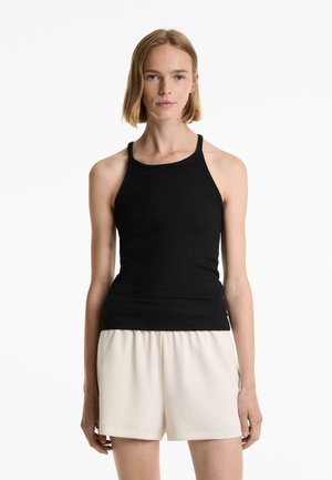 Svart ribbad linne med smala axelband, figursydd design och mjuk textur. Kombinerat med ljusbeiga shorts, vilket skapar en kontrasterande look.