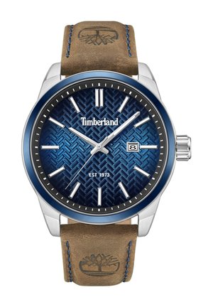 Reloj Timberland con un dial azul estampado, caja de acero inoxidable plateada, display de fecha y correa de cuero marrón con un logo en relieve.