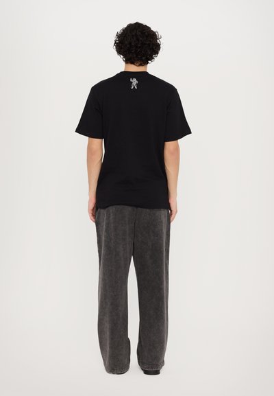 T-shirt en coton noir à manches courtes avec un petit graphique blanc au dos, associé à un pantalon large gris avec une finition douce et texturée.