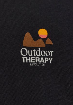 Zwarte katoenen t-shirt met een tan bergen graphic en een zonsondergang in roze en geel. Tekst leest "Outdoor THERAPY REVOLUTION."