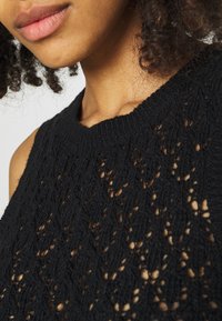 Schwarzes, gestricktes, ärmelloses Oberteil mit einem strukturierten Spitzenmuster, geripptem Halsausschnitt und einer lässigen Passform um Schultern und Hals.