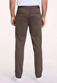 Braune, schlanke Hosen mit glatter Textur, ausgestattet mit zwei Gesäßtaschen, einem Bund mit Gürtelschlaufen und zuspitzenden Beinen, kombiniert mit weißen Turnschuhen.