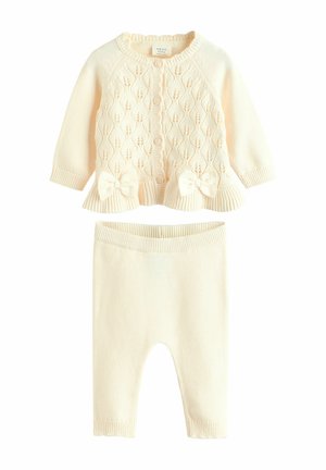 Kremfarvet strikket babycardigan med knapper foran, dekorative sløjfer, matchende strikkede leggings, ribstrikkede manchetter og linning.