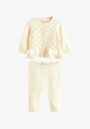 Kremfarvet strikket babycardigan med knapper foran, dekorative sløjfer, matchende strikkede leggings, ribstrikkede manchetter og linning.