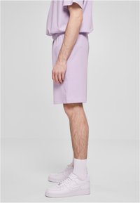 Lilla bomullst-skjorte og matchende shorts, avslappet passform, elastisk midjebånd, kombinert med hvite joggesko og sokker. Enkel, helhetlig look.