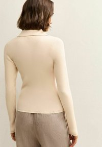 Maglione crema a coste con collo, maniche lunghe e design aderente, abbinato a pantaloni beige a quadri con una texture morbida.