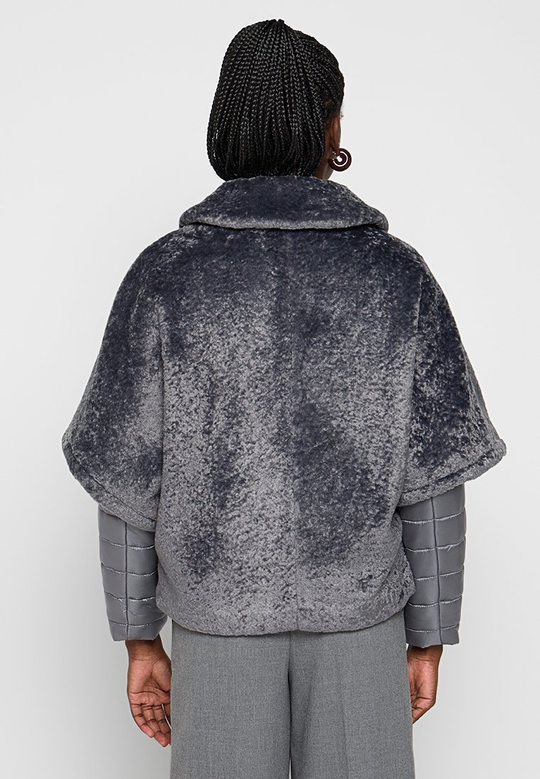 Grau Kunstfellmantel mit großem Kragen, weiten Ärmeln und einer strukturierten, weichen Oberfläche. Der Mantel ist mit einem grauen gepolsterten Innensleeve gestylt.