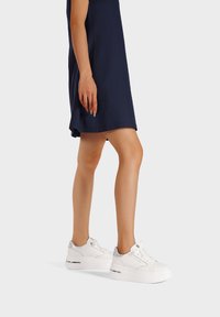 Sneakers platform bianchi con accenti argento e lacci alla moda, indossati con un abito blu navy, che mettono in mostra una texture liscia e un design moderno.