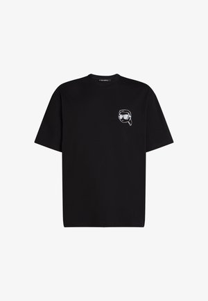 Melnas kokvilnas T-krekls ar mazu balto izšuvumu, kurā redzama seja ar saulesbrillēm kreisajā krūšu daļā. Apaļa apkakle.