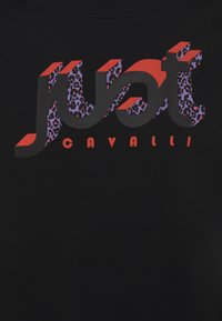 Tissu noir avec un texte 3D "Just" en gras aux bords rouges et imprimé léopard violet, avec "Cavalli" en lettres majuscules rouges en dessous.