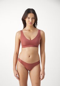Brun bh och matchande bikini, tillverkad av slätt tyg. Bh:n har en djup V-ringning och breda remmar; bikinin har låg midja och minimal täckning.