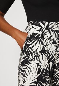 Musta-valkoinen palmunlehden kuvioinen kangas, jossa on sileä tekstuuri. Korkeavyötäröisessä mallissa on laskokset ja sivutaskut.