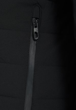 Zbliżenie pionowego zamka błyskawicznego czarnej kurtki z dużym, fakturowanym uchwytem na pikowanym materiale.