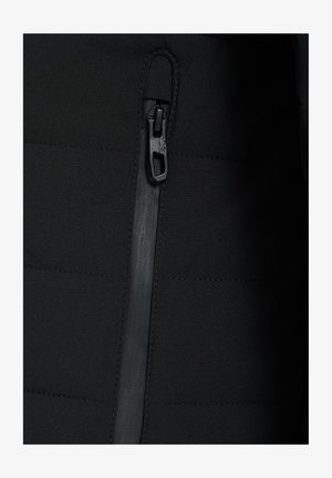 Zbliżenie pionowego zamka błyskawicznego czarnej kurtki z dużym, fakturowanym uchwytem na pikowanym materiale.