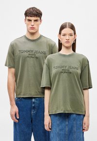 Tricouri de bumbac verde măsliniu cu croială lejeră, având brodate textele "TOMMY JEANS" și "New York City" pe partea din față.