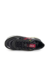 Schwarzer Sportschuh mit strukturiertem Oberflächenmaterial, ausgestattet mit roten Akzenten und gelben Schnürösen. Das Design umfasst eine gepolsterte Sohle und ein genähtes Muster.